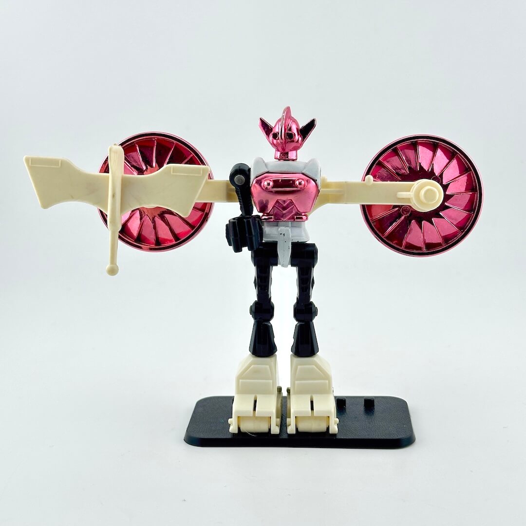 White, black, and pink toy robot with beige accessories on white background. 