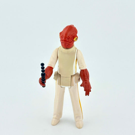 Action figure with red head and beige outfit holding a black and black weapon on a light gray background