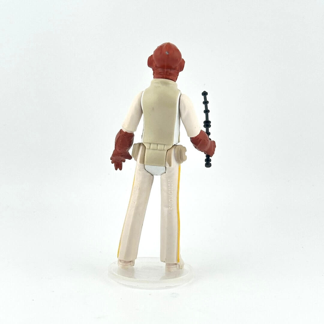 Action figure with red head and beige outfit holding a black and black weapon on a light gray background