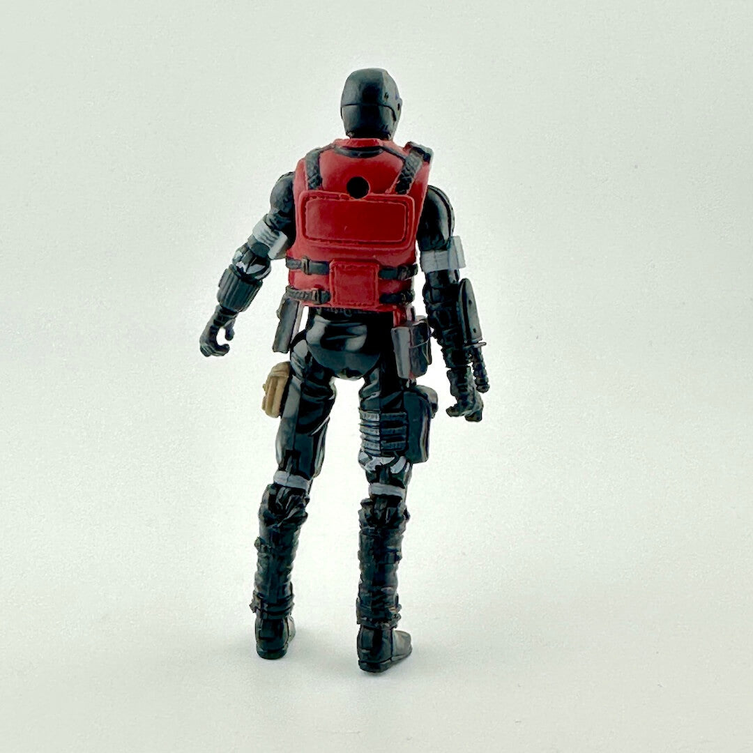 A back view of a black and red action figure with tactical gear, standing against a plain light gray background.
