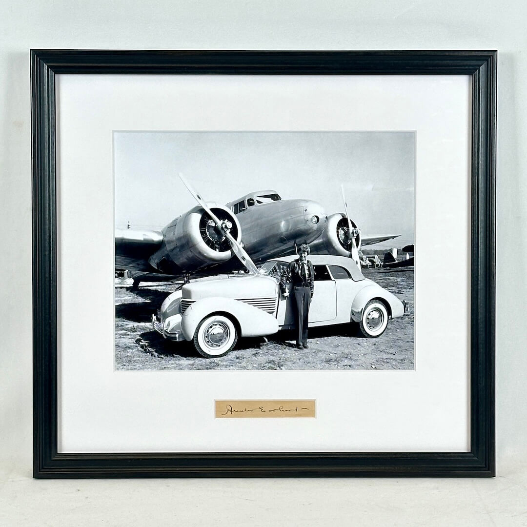 Framed black and white photograph of a car and airplane with a person standing next to the car.