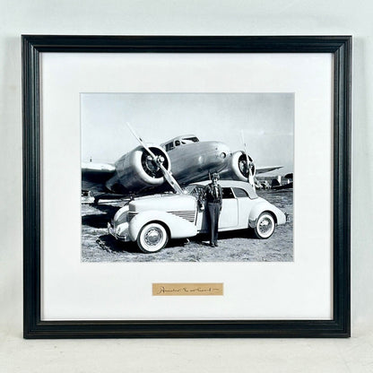 Framed black and white photograph of a car and airplane with a person standing next to the car.