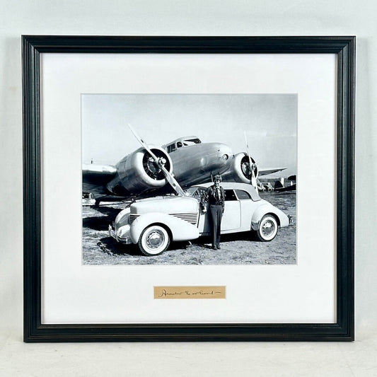 Framed black and white photograph of a car and airplane with a person standing next to the car.