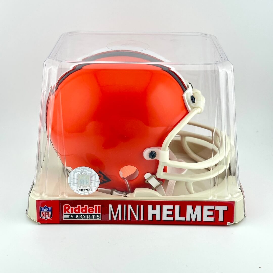 Orange mini football helmet in clear packaging with Riddell Sports branding on a white background