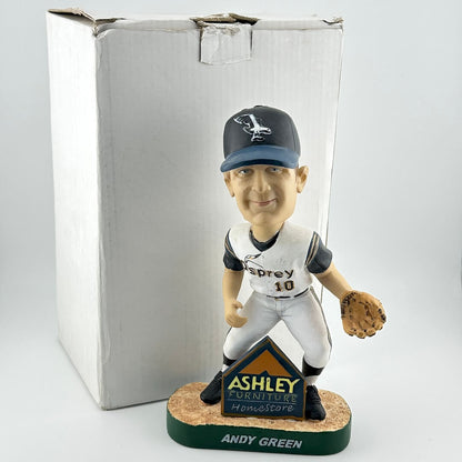 Baseball bobblehead figure with a cap and glove, standing on a base with branding, in front of a branded box.