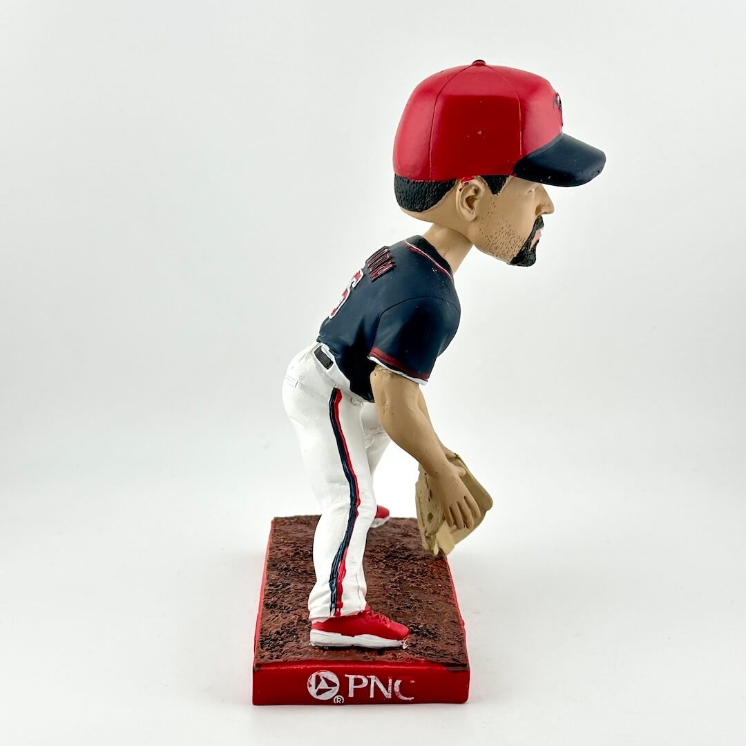 Baseball bobblehead figure with red and blue cap, navy jersey, and white pants on a white background.