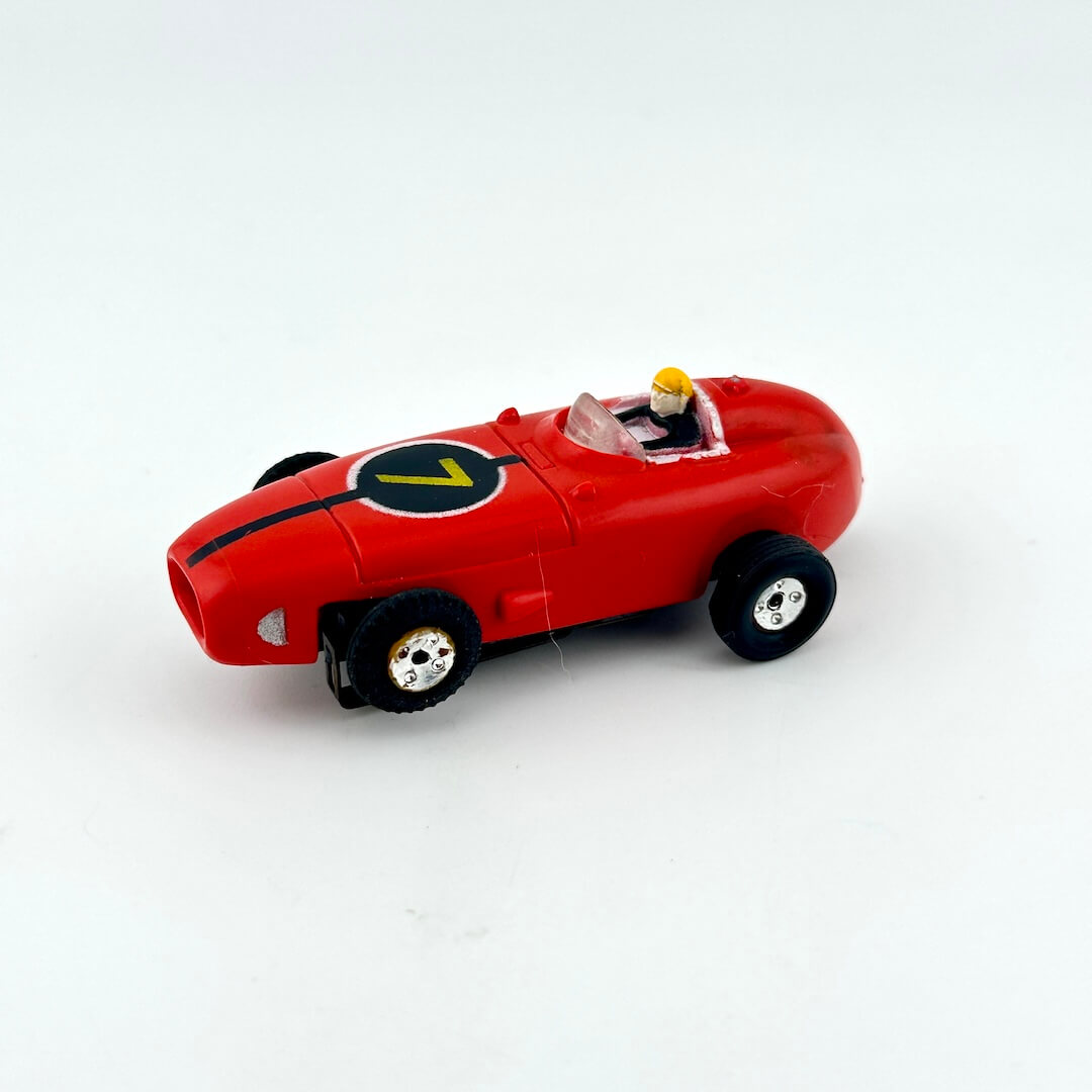 Red slot car with driver against white background.