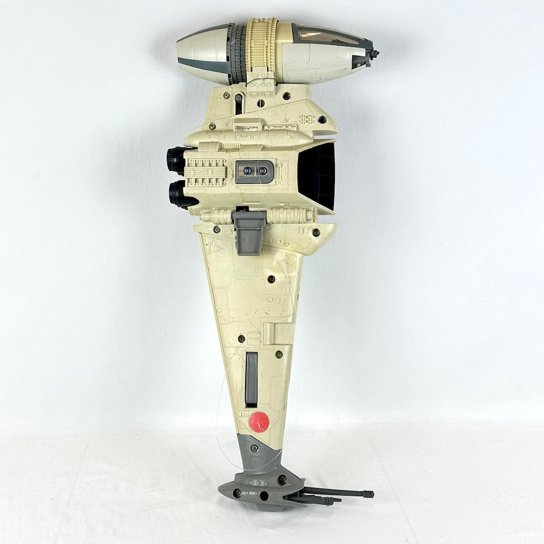 A vintage Star Wars toy spaceship, specifically a B-Wing fighter, in a light beige and gray color scheme.