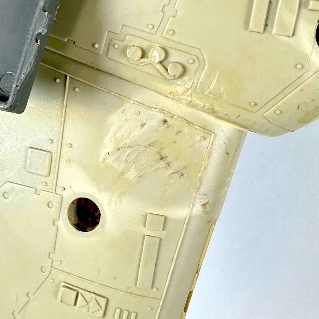 Close-up of a beige plastic model part with molded details, scratches, and a small dark opening.