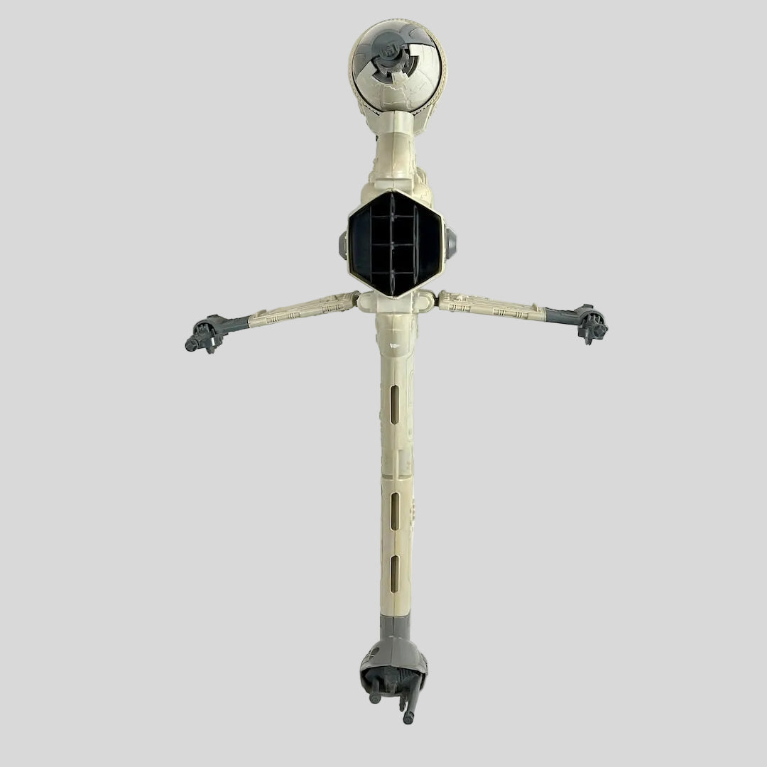A vintage plastic toy spaceship with a cream-colored body, gray arms and legs, and a black central panel.