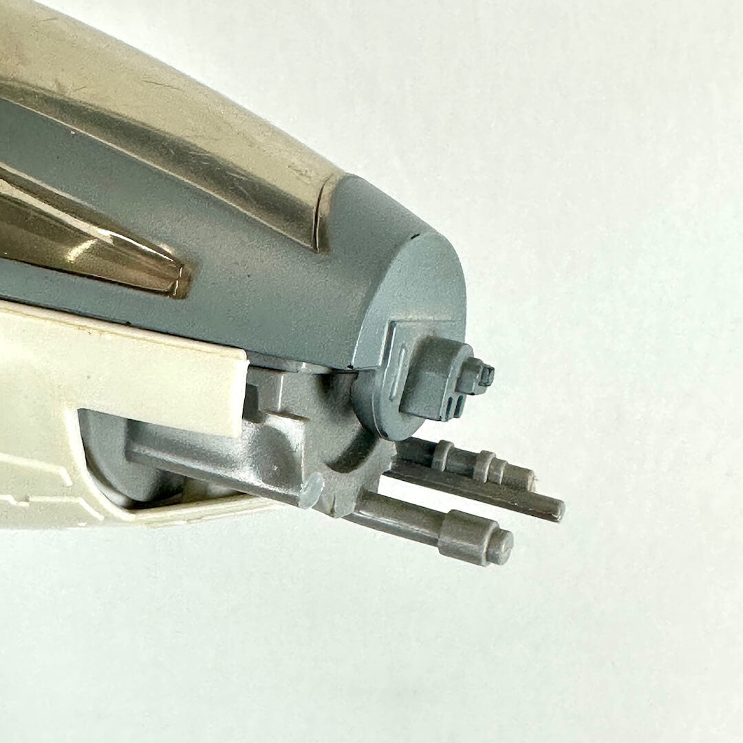 Close-up of a model vehicle or toy part, showing a gray and metallic nose section with small protruding rods.