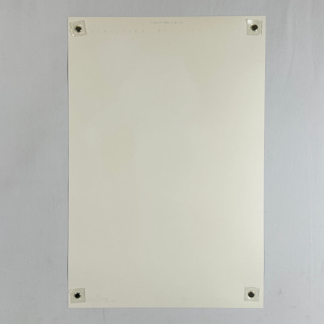 Backside of cream colored poster with no visible damage being held by magnets in the corners against light surface. 