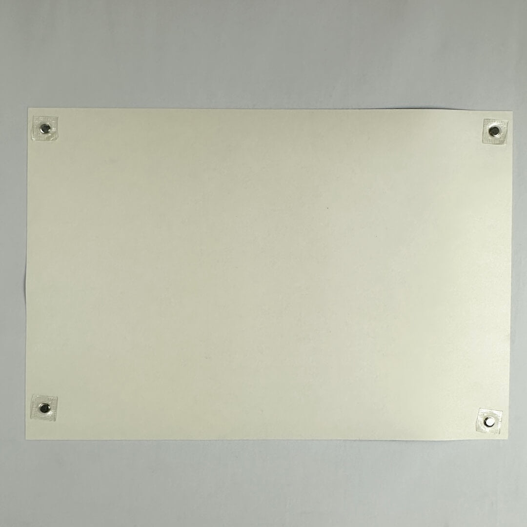 Backside of cream-colored poster showing no damage and being held by magnets in each corner against a light surface. 