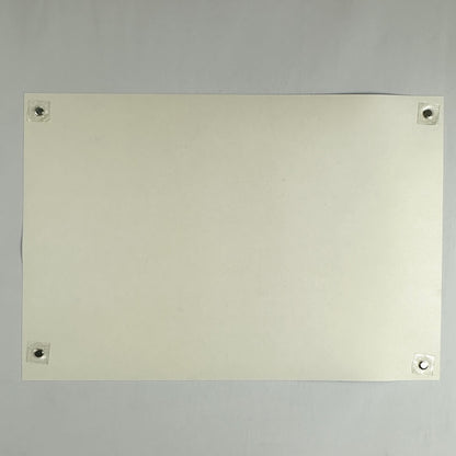 Backside of cream-colored poster showing no damage and being held by magnets in each corner against a light surface. 