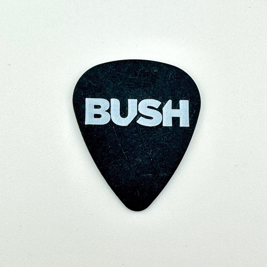 Black guitar pick with white text, "BUSH" photographed against white background. 