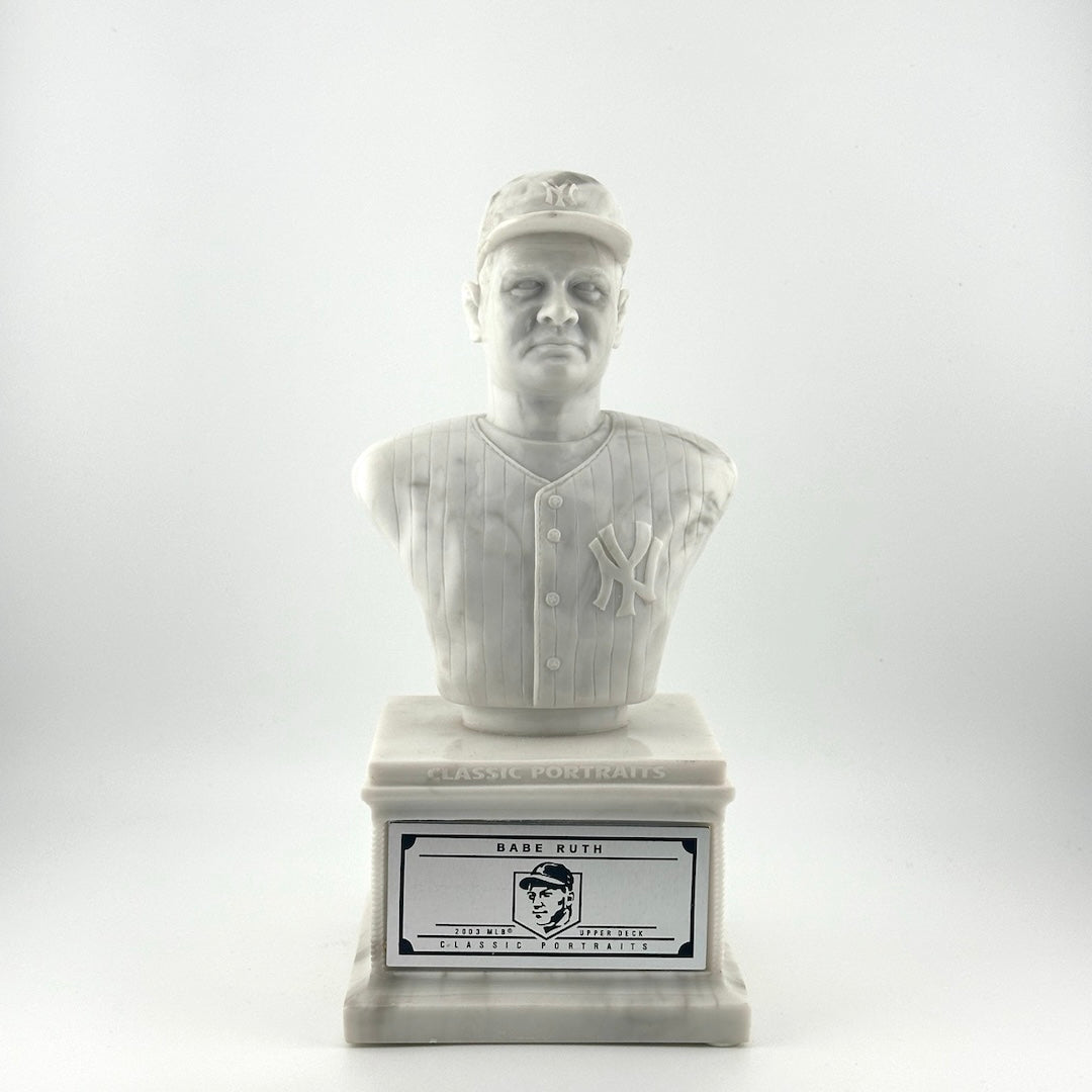 Marble pedestal with marble bust of Babe Ruth in Yankees uniform. Silver plaque on pedestal.