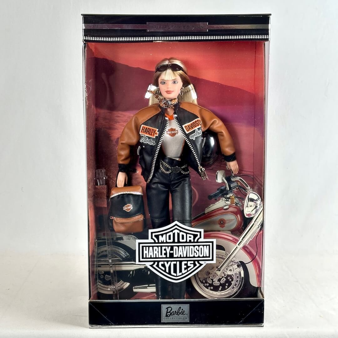 A Barbie doll dressed as a Harley-Davidson rider, standing inside its original retail packaging. 