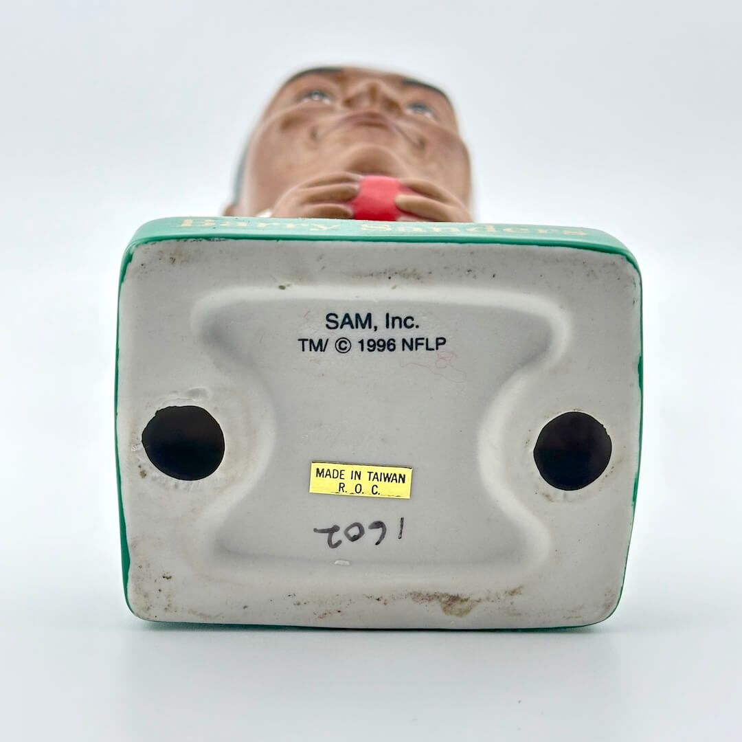 Under view of a toy figure with 'SAM, Inc.' branding and product details on a white background.