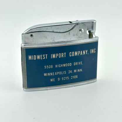 A vintage silver metal lighter with a dark blue enamel side panel printed with the address of Midwest Import Company, Inc.
