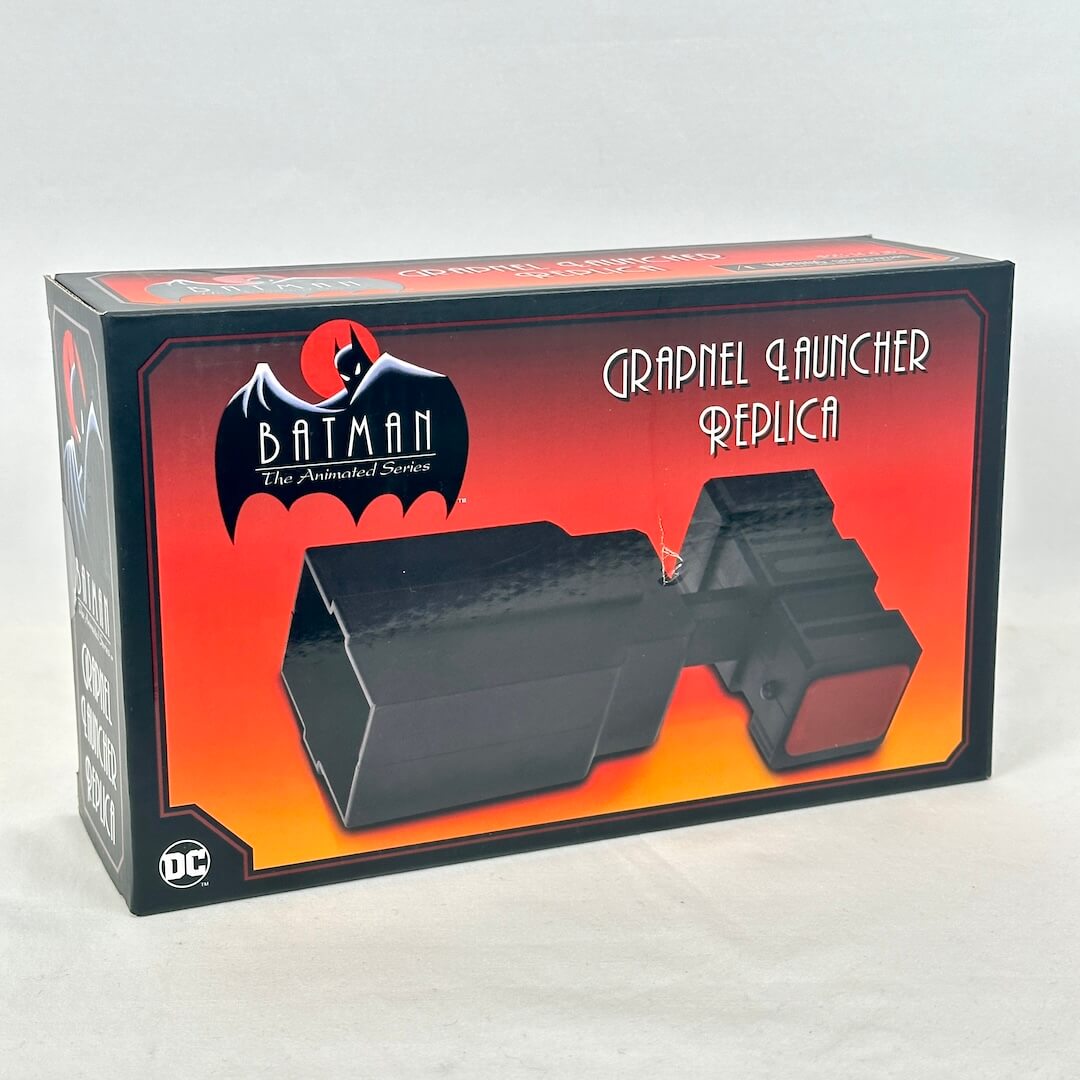 A boxed replica of the Grapnel Launcher from Batman: The Animated Series, shown in its retail packaging.