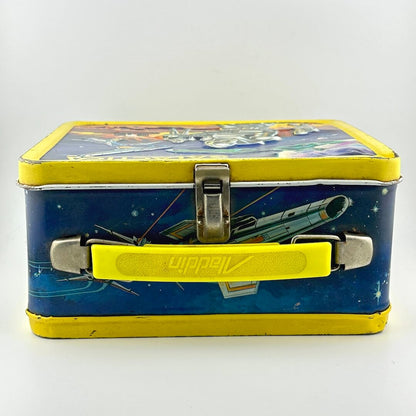 Top view of metal lunchbox with yellow plastic handle, yellow borders, blue background with spaceship illustration. 