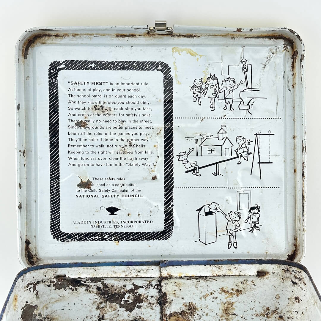 View of interior lid of vintage metal lunchbox showing safety instructions with illustrations. 