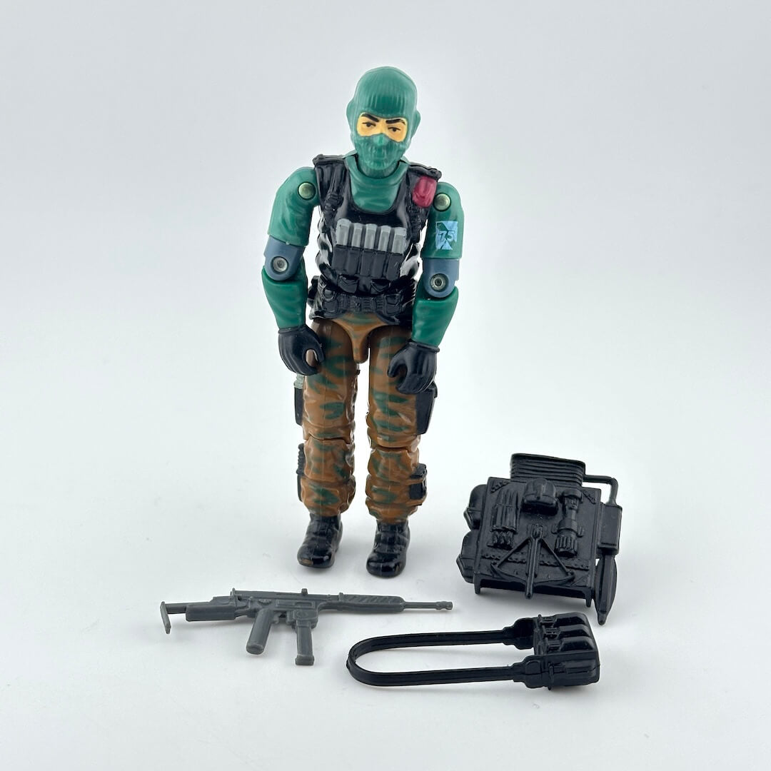 A G.I. Joe action figure in green and brown, standing next to three accessories on white background. 