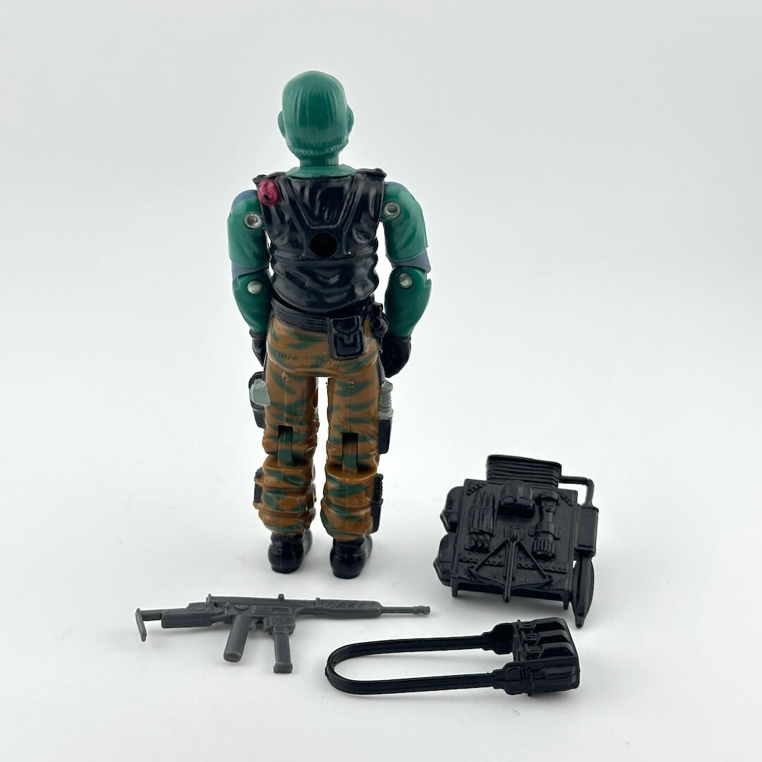 A vintage action figure shown from the back, wearing a green helmet and torso, black vest, and brown camouflage pants.