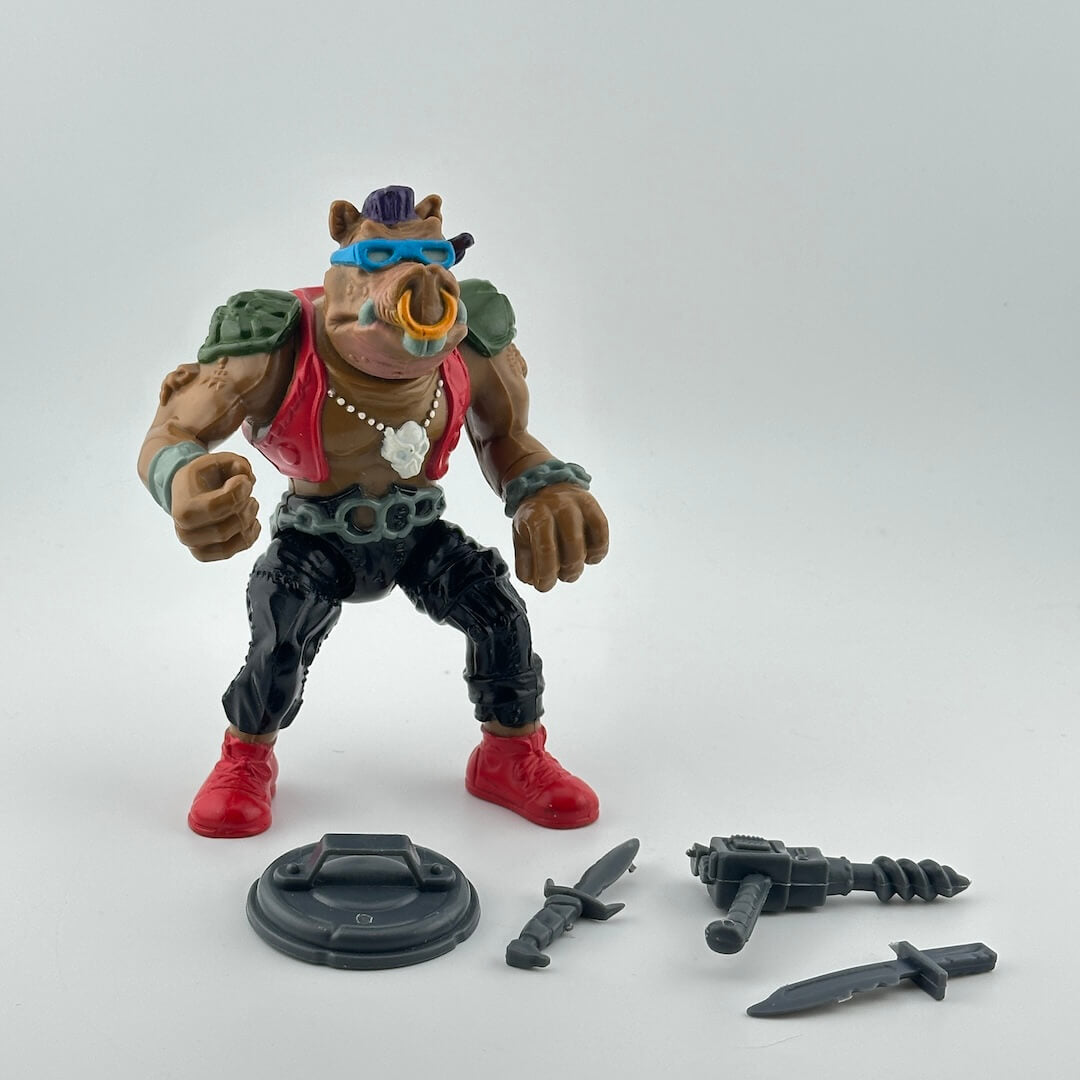 Anthropomorphized hog in black pants, red vest, blue sunglasses, chain belt, piercing through nose is shown with gray accessories. 