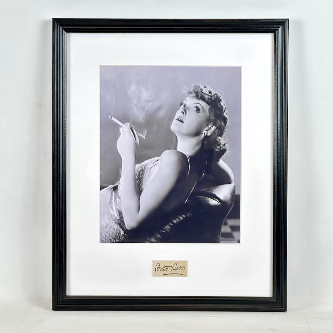 A framed black and white portrait print of a woman smoking, mounted with a wide white mat and a black frame.