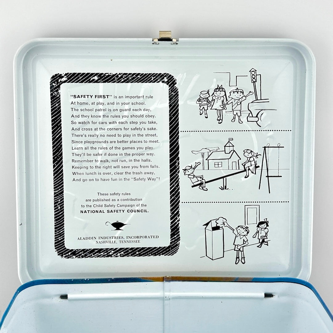 An open vintage metal lunchbox, showing printed safety instructions on the inside lid and simple line drawings of children.