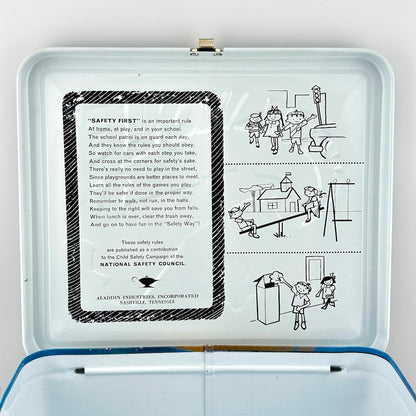 An open vintage metal lunchbox, showing printed safety instructions on the inside lid and simple line drawings of children.