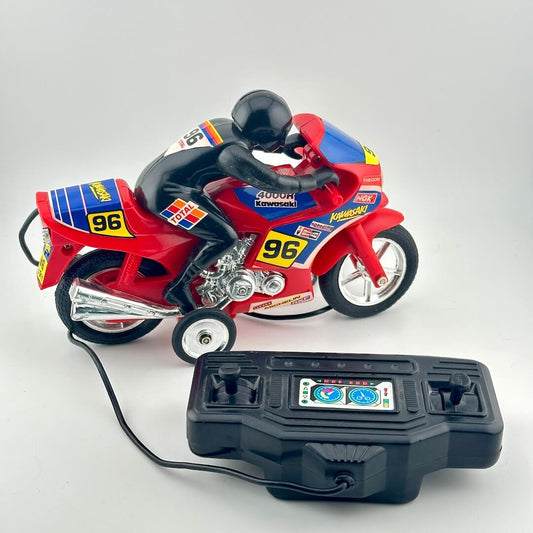 A red toy racing motorcycle with a black rider figure, shown with a black remote control on a light gray background.
