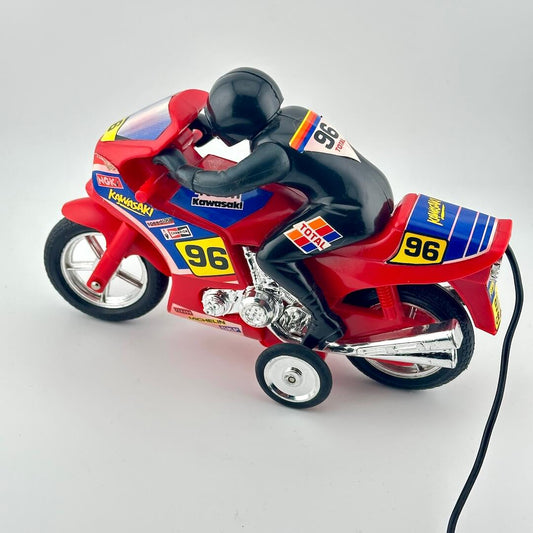 A red and blue toy motorcycle with training wheels, featuring a black racer figure on top, photographed on a light gray background.