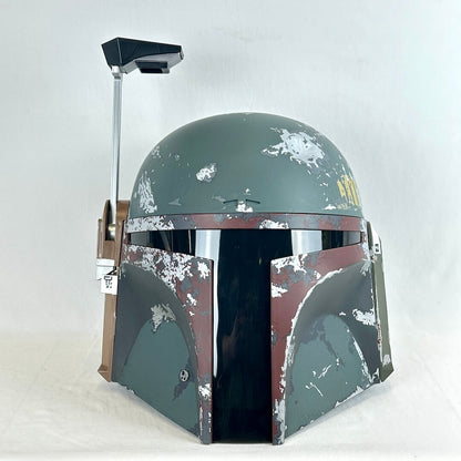 A Boba Fett style sci-fi helmet replica with a distressed green and brown paint scheme, shown against a plain light gray background.