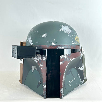 A distressed Boba Fett style helmet replica, featuring a weathered green-gray and brown paint scheme.