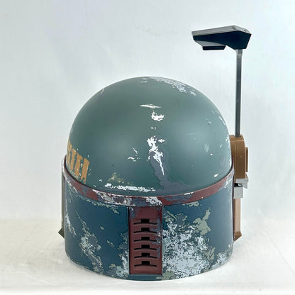 A distressed Boba Fett style sci-fi helmet replica, featuring a weathered green-gray dome, and rust-red band.