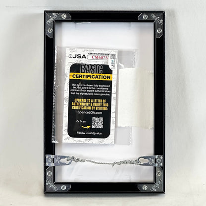 A black picture frame with decorative corner brackets and a hanging chain, containing a white certificate insert with a JSA Basic Certification card.
