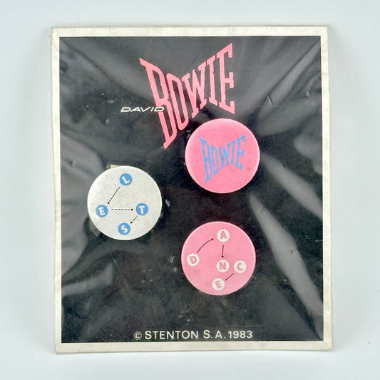 Black card with David Bowie branding with three circular pins in white and pink color scheme. 