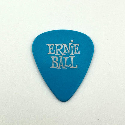 Blue guitar pick with silver text, "Ernie Ball" photographed against white background. 