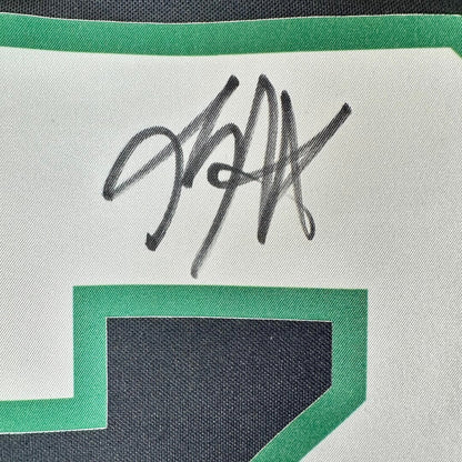 Close-up of a white sports jersey with a green border and a black autograph in the center.