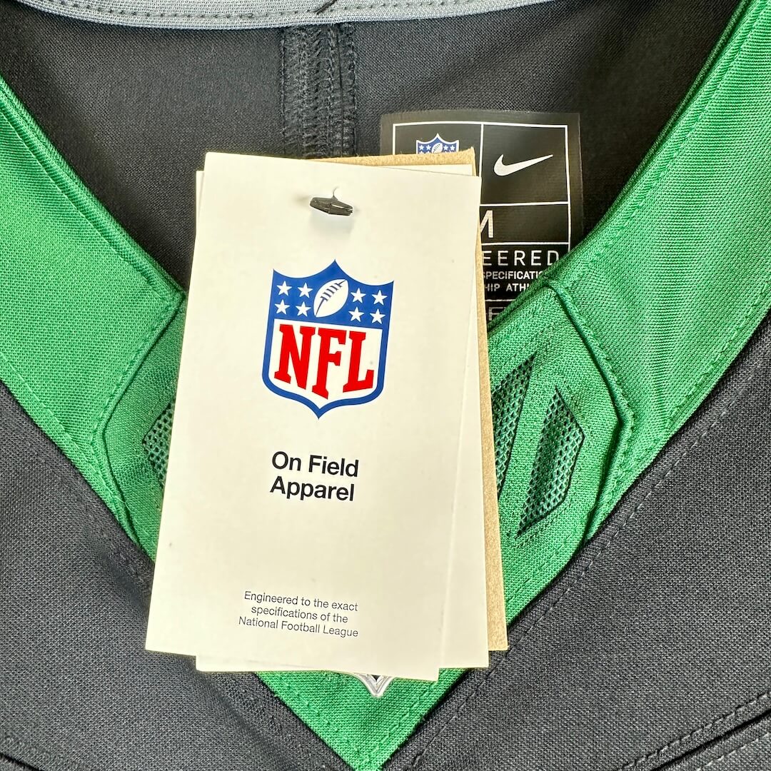 Close-up of a Nike NFL jersey with a visible NFL On Field Apparel hangtag and a Nike tag inside the collar. 
