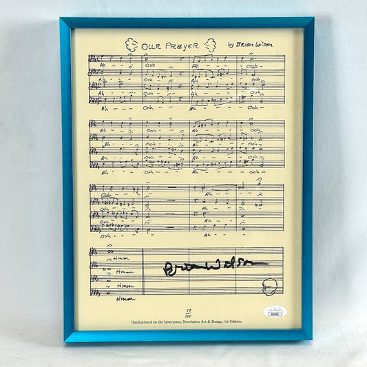 A turquoise framed sheet of music signed by Brian Wilson with authentication sticker at bottom right. 
