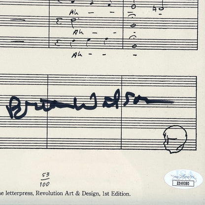 A close-up of a printed sheet music page with musical notation, handwritten musical notes, a signature, and an authentication sticker in the lower right corner.