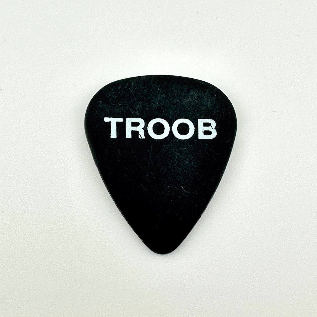 A black guitar pick with the word 'TROOB' printed in white capital letters, centered on a plain light background.