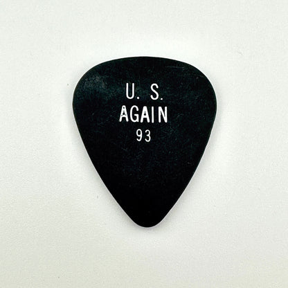 A black guitar pick with white printed text reading 'U. S. AGAIN 93' in the center, shown on a plain light background.
