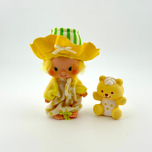 Toy figure of a girl with a yellow hat and dress, standing next to a toy bear on a white background