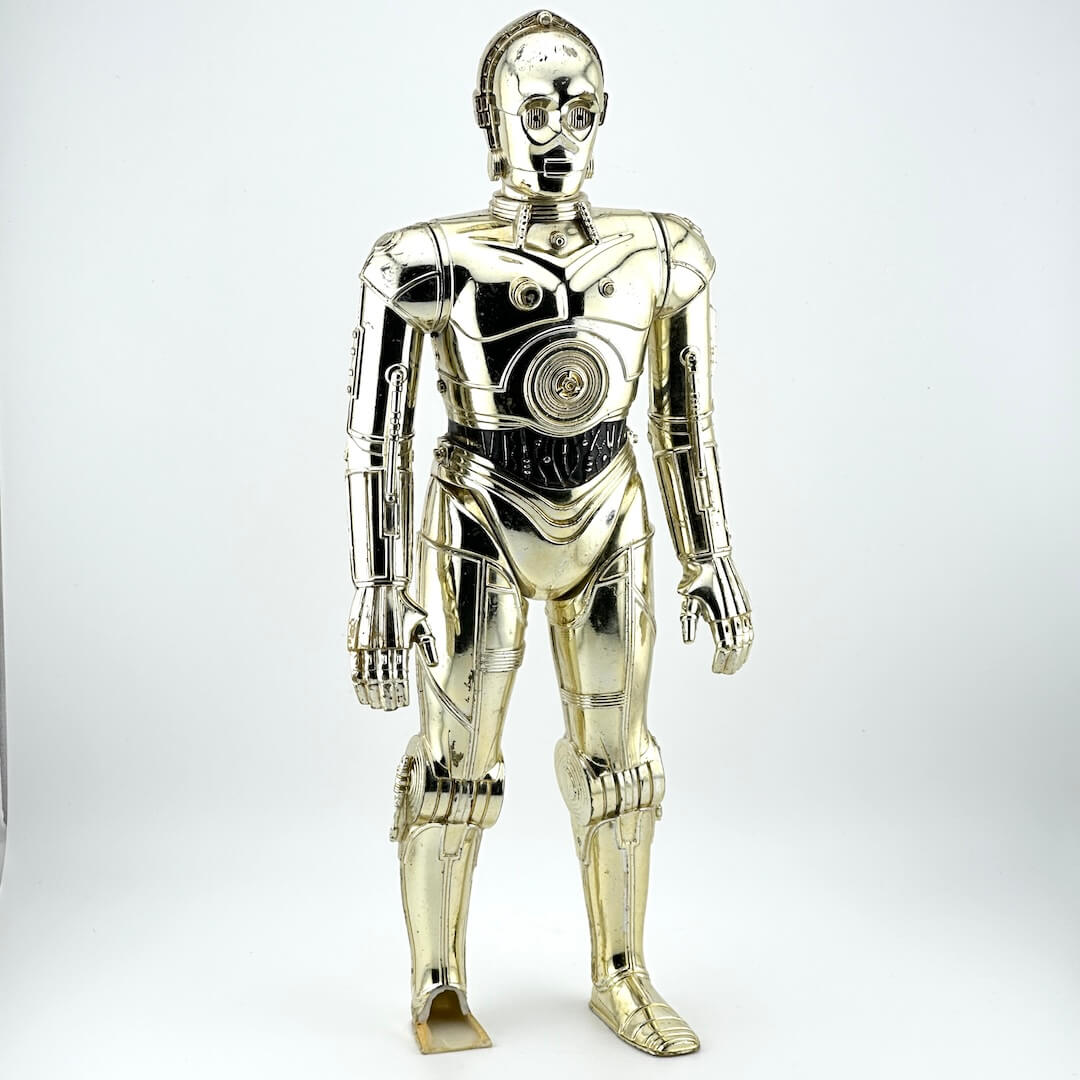 Plastic figure of gold/silver robot with broken left foot against white background. 