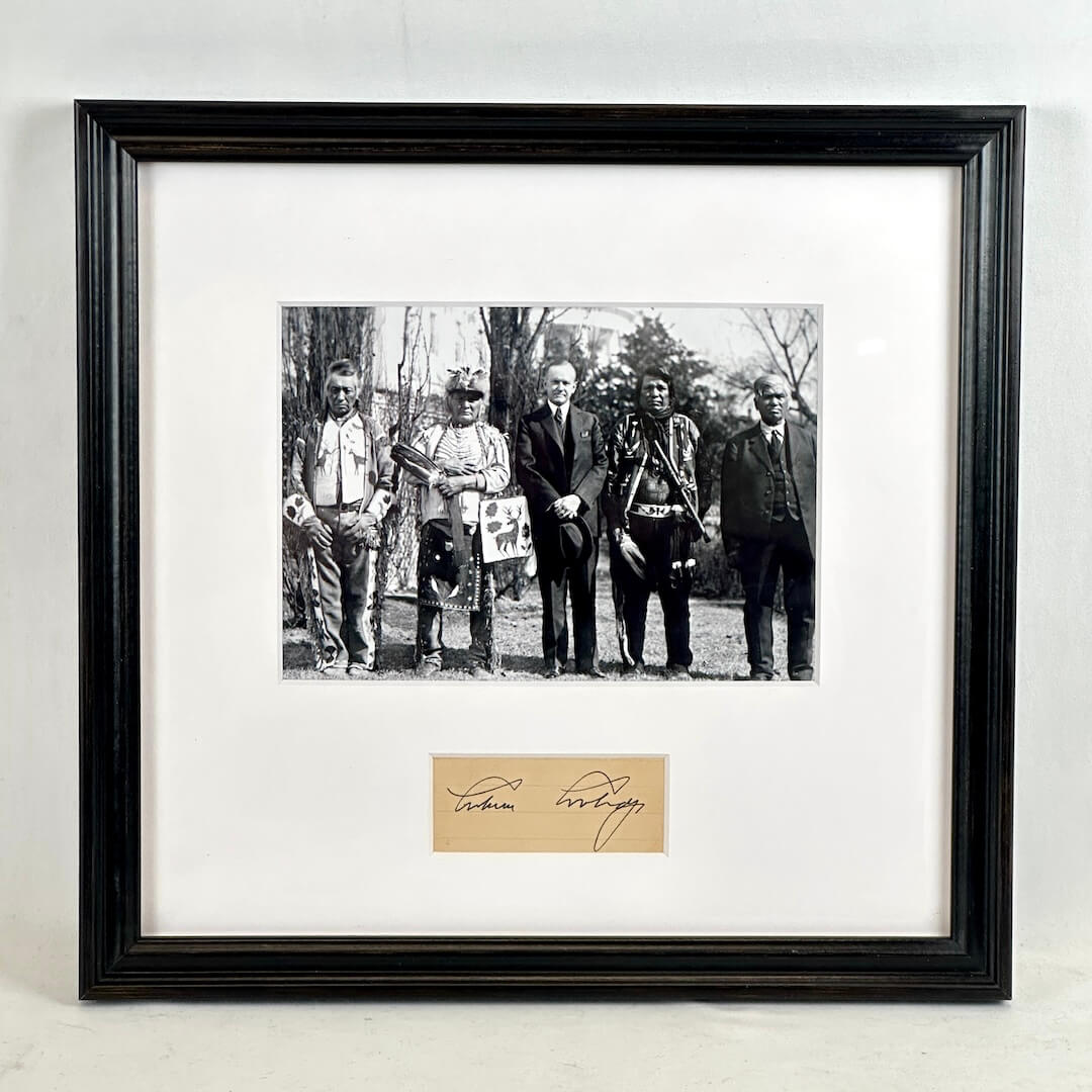 A framed black-and-white historical photograph print with a white mat and a black frame, with an autograph card mounted below