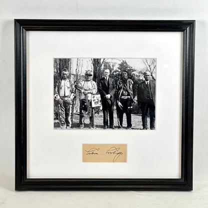 A framed black-and-white historical photograph print with a white mat and a black frame, with an autograph card mounted below